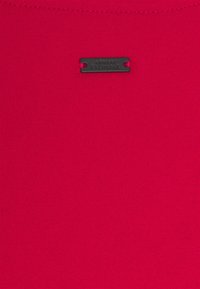 Jasnoróżowy materiał o prążkowanej fakturze, z czarną metaliczną metką z wytłoczonym napisem "ARMANI EXCHANGE".