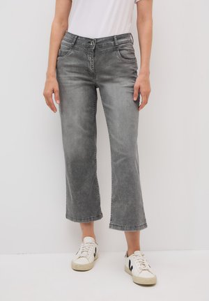 Jean en denim gris, coupé court avec une coupe droite, délavage subtil, cinq poches et fermeture à bouton, associé à des baskets blanches.