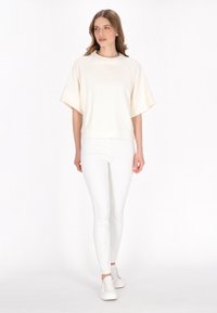 Felpa oversize di colore crema chiaro con maniche raglan, abbinata a pantaloni bianchi slim-fit e sneaker bianche. Design semplice, texture morbida.