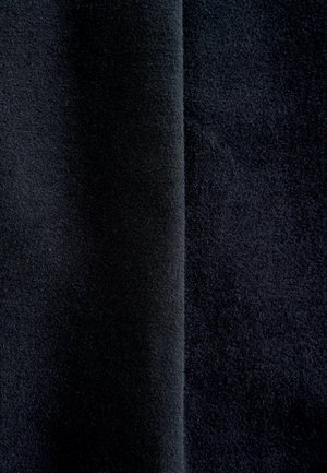 Tessuto nero con una superficie morbida e textrurata, caratterizzato da un pelo denso e una leggera lucentezza, piegato per evidenziare la sua profondità e il colore uniforme.