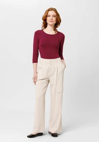 Bordeaux langetuig bodysuit gecombineerd met crème wijde hoge taille broeken met een zijvak. Model draagt zwarte ballerina's.