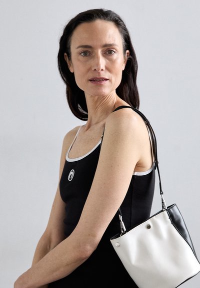 Črn top s tanki belimi naramnicami vsebuje okrogel logotip. Dvobarvna torba združuje bele in črne materiale, s sleek dizajnom in nastavljivim trakom.
