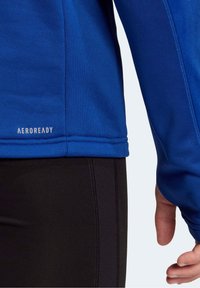 Maglietta sportiva blu a maniche lunghe con una superficie liscia, branding AeroReady e tessuto nero a contrasto in vita.