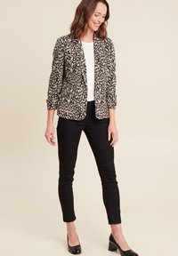 Luipaardprint blazer met een gestructureerd ontwerp, lange mouwen en zwarte accenten, gecombineerd met zwarte strakke broeken en glanzende zwarte hakken.