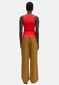 Rotes, geripptes Tank-Top kombiniert mit hoch taillierten, braunen, weiten Hosen, von hinten betrachtet. Die Hose hat eine glatte Textur und einen lockeren Sitz.