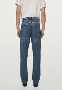 Jeans in denim blu con taglio a gamba dritta, dotati di due tasche posteriori e una toppa in pelle marrone sulla cintura. Design standard con cinque tasche.