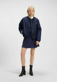 Granatowa bomberka o gładkiej fakturze, z zamkiem błyskawicznym i bocznymi kieszeniami. Połączona z dopasowaną granatową sukienką i czarnymi botkami za kostkę.