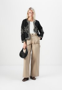 Quilted black jacket with white embroidery, paired with a white top, beige wide-leg trousers, and leopard print flats. Holds a black bag.