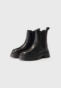 Een paar zwarte leren Chelsea-boots met dikke profielzolen en trekbandjes, getoond op een egale lichte achtergrond.