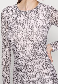 Długie rękawy, siatkowa bluzka z powtarzającym się czarno-białym wzorem logo na jasnoróżowym tle, z klasycznym okrągłym dekoltem.