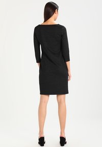 Czarna sukienka z trzema ćwierć rękawami, o prostym kroju, z fakturowanej tkaniny i dekoltem typu łódka, sięgająca powyżej kolan. Noszona z czarnymi szpilkami.