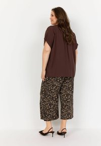 Hnedý krátky rukáv top v kombinácii s čiernymi skrátenými nohavicami so zvieracou potlačou. Čierne lodičky dodávajú outfitu dokonalý vzhľad.