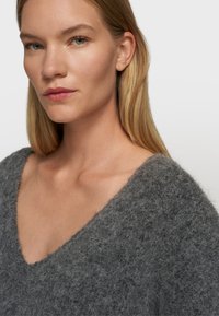 Grauer Wollpullover mit tiefem V-Ausschnitt und strukturierter, flauschiger Oberfläche. Nahaufnahme, die den Ausschnitt und das weiche, warme Erscheinungsbild hervorhebt.