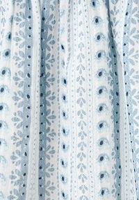 Plis verticaux en tissu avec des motifs floraux bleus et blancs ainsi que des pois, alternant en bandes sur un fond clair.
