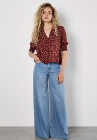 Blusa con stampa floreale rossa, scollo a V e maniche corte a sbuffo, abbinata a jeans a palazzo leggeri e azzurri, che presentano una vestibilità comoda e due tasche.