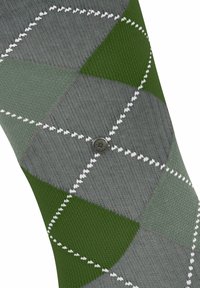 Grüne und graue Argyle-Socke mit weißen Nähten, ausgestattet mit einem metallenen Knopfdetail. Strukturiertes Strickmaterial, geneigtes Design.