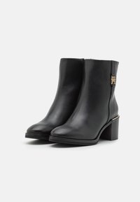 Botas de tobillo de cuero negro con un acabado suave, punta redondeada, tacón medio y detalles de hardware en tono dorado.