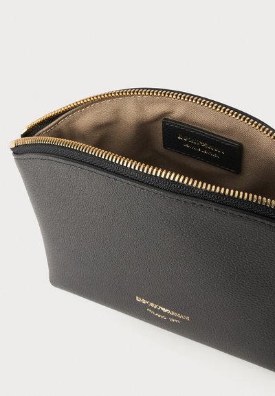 Μαύρο θήκη Emporio Armani με χρυσό φερμουάρ μερικώς ανοιχτό, που δείχνει εσωτερικό από μπεζ ύφασμα και ετικέτα μέσα.
