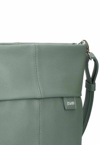 Borsa a tracolla in pelle verde con un design strutturato, parte superiore pieghevole, cuciture in vista, tracolla regolabile e una piccola etichetta con logo.