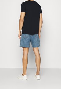 Camiseta negra de algodón, pantalones cortos de mezclilla azul y zapatillas blancas. Los pantalones cortos tienen bolsillos y un dobladillo deshilachado, la tela tiene una textura suave.