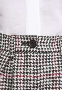 Hoge taille broek met een houndstooth patroon in zwart, wit en rood, voorzien van een zwarte knop op de tailleband en geplooide details.