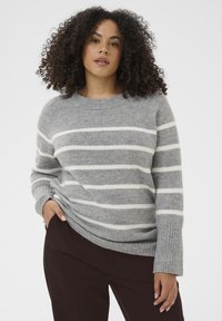 Pull en laine gris à rayures, fabriqué en matériau doux, avec de larges rayures blanches, un col rond et des poignets côtelés, associé à un pantalon sombre.