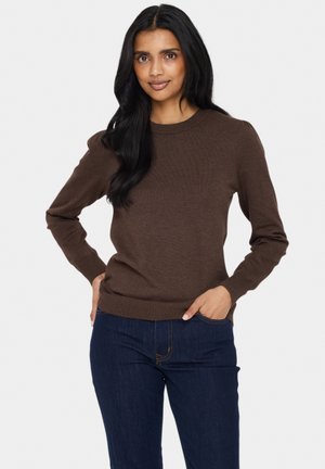 Bruine gebreide trui met een ronde hals, lange mouwen en geribbelde manchetten en zoom. Gepaard met donkerblauwe denim jeans.