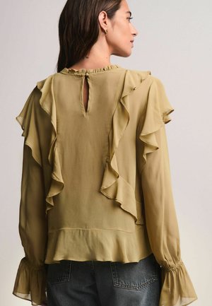 Olivgrüne Bluse aus leichtem Stoff mit rüschierten Lagen entlang der Vorderseite und Ärmel. Detail mit Schlüsselloch am Rücken und ausgestellten Manschetten.