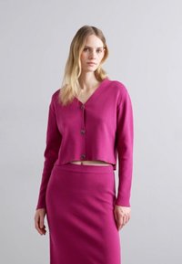 Fuchsia verkürzte Strickjacke mit langen Ärmeln, Knopfschluss und passendem hochgeschnittenen Rock. Glatte Textur, schlichtes Design, keine Muster.