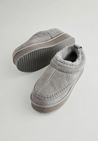 Grå ruskinds slippers med en blød grå pelsforing, rund tå, syninger og en struktureret gummisål.