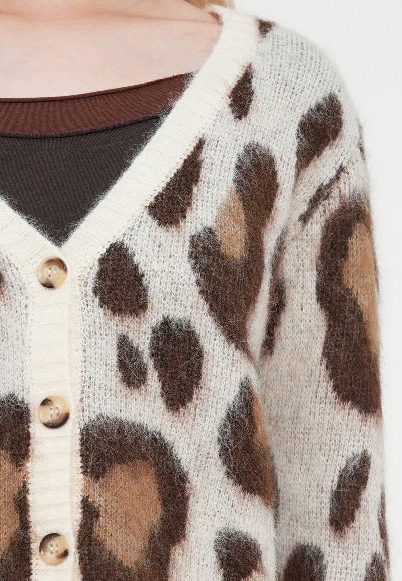 Sweter cardigan z kremowym tłem w brązowe i beżowe plamki w stylu lamparta, dekolt w kształcie V, prążkowane krawędzie oraz duże, zaokrąglone drewniane guziki.
