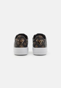 Svarta sneakers med präglade gyllene mönster, vit gummisula och triangulärt logobadge på baksidan. Texturerad läderfinish.