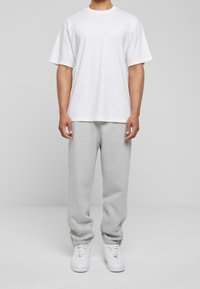 Weißes Baumwoll-T-Shirt mit kurzen Ärmeln, kombiniert mit hellgrauen Jogginghosen und weißen Turnschuhen. Einfaches Design, lockere Passform, keine sichtbaren Logos.