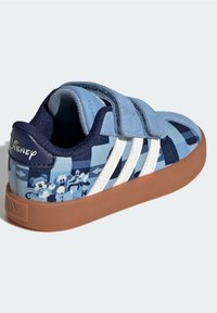 Blå kanvas sneakers med vita ränder, kardborreband och mönster av tecknade figurer på en strukturerad yta. Sula av gummigummi.