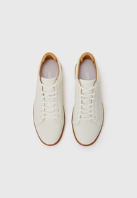 White leather sneakers with a textured finish, featuring round toe, contrasting tan interior, and standard lace-up closure.