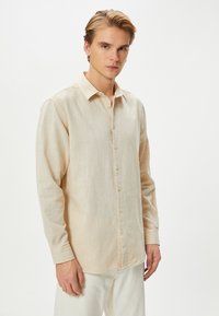 Lichtbeige overhemd met lange mouwen, gemaakt van textuurstof, met een knoopsluiting aan de voorkant, klassieke kraag en zacht gebogen zoom.
