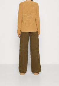 Maglione a maglia color cammello con un motivo testurizzato e maniche raglan, abbinato a pantaloni cargo a gamba larga verde oliva con cinturini sul ginocchio.