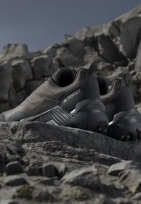 Para czarnych butów trekkingowych Adidas Terrex ustawiona na skalistym terenie pod czystym niebem.