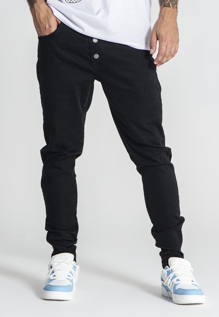 Jeans negros ajustados con cierre de botón de metal y diseño de cinco bolsillos, combinados con zapatillas blancas con acentos azul claro.