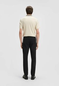 Beige short-sleeve polo shirt with a patterned collar, paired with black straight-leg trousers and black shoes, viewed from the back.
