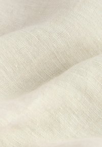 Tela de lino natural en un suave color crema, que muestra un tejido texturizado con fibras visibles y una superficie ligeramente brillante.