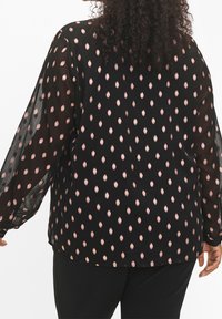 Blusa nera con maniche trasparenti, caratterizzata da un motivo di ovali rosa. Fit morbido con orlo arrotondato e maniche con polsini.