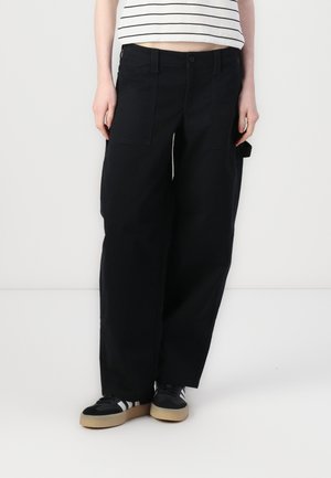 Pantalons cargo noirs avec une coupe décontractée, dotés de poches latérales, d'une fermeture à bouton et de passants de ceinture, associés à des baskets noires et blanches.