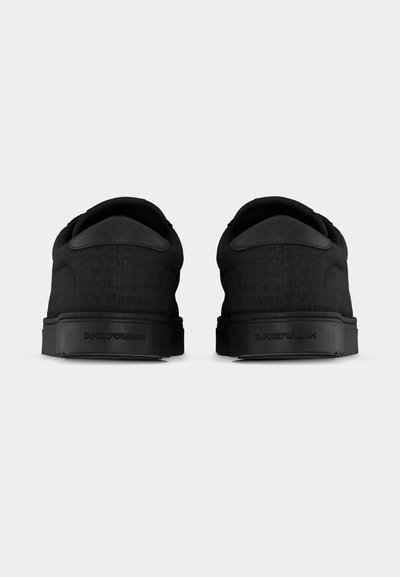 Ζευγάρι μαύρα sneakers χαμηλής κορυφής με ανάγλ υφη σήμανση Emporio Armani στη φτέρνα και υφή στην επάνω επιφάνεια, μέσα από την πίσω όψη, σε λευκό φόντο.