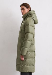 Olijfgroen pufferjas met een capuchon, voorzien van een rits, gebreid textuur en ribgebreide accenten bij de manchetten, tot halverwege de kuit.