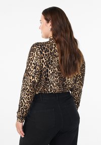 Dug madža s dugim rukavima u uzorku leoparda s nijansama bež i crne; kombinira se s hlačama visokog struka u crnoj boji; glatka tekstura tkanine.