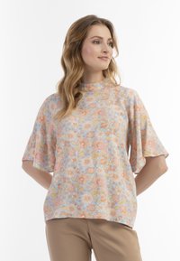 Blusa floreale in colori pastello con maniche corte a campana. Presenta un collo alto e un tessuto leggero e testurizzato con un vivace motivo floreale.