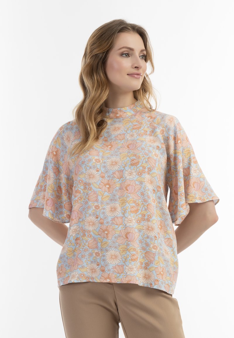 Blusa floreale in colori pastello con maniche corte a campana. Presenta un collo alto e un tessuto leggero e testurizzato con un vivace motivo floreale.
