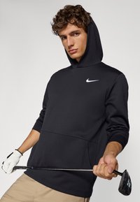 Black Nike hooded sweatshirt with a textured finish, featuring a front pocket and a white logo on the chest, paired with a golf club.