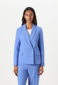 Lys blå skreddersydd blazer med sjalkrage, dobbeltradet front, to klafflommer og lange ermer. Glatt stoff med en strukturert passform.